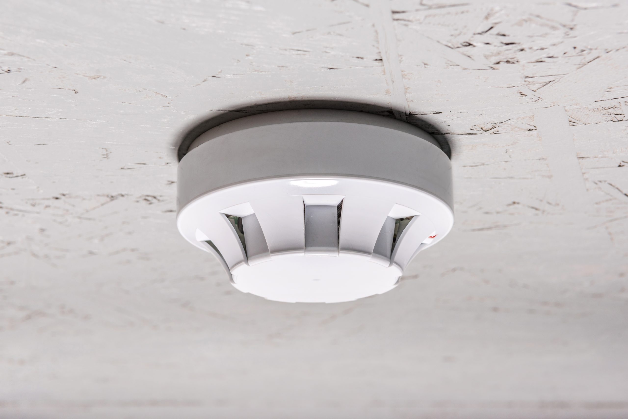 Smoke detector of fire alarm on white ceiling at h